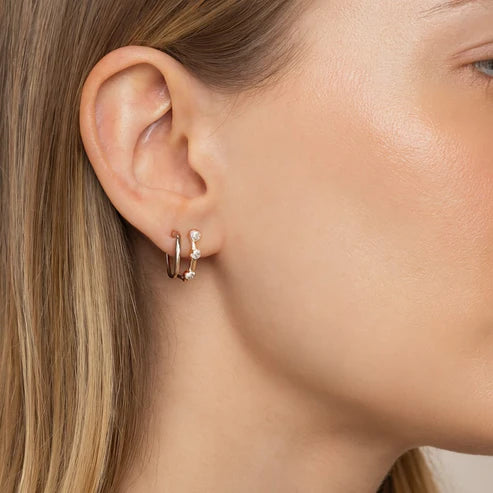 Close-up of a person wearing gold hoop earrings with small clear stones.