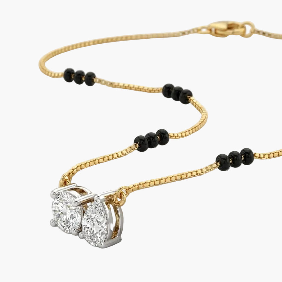 Gold necklace with black beads and a diamond pendant on a white surface