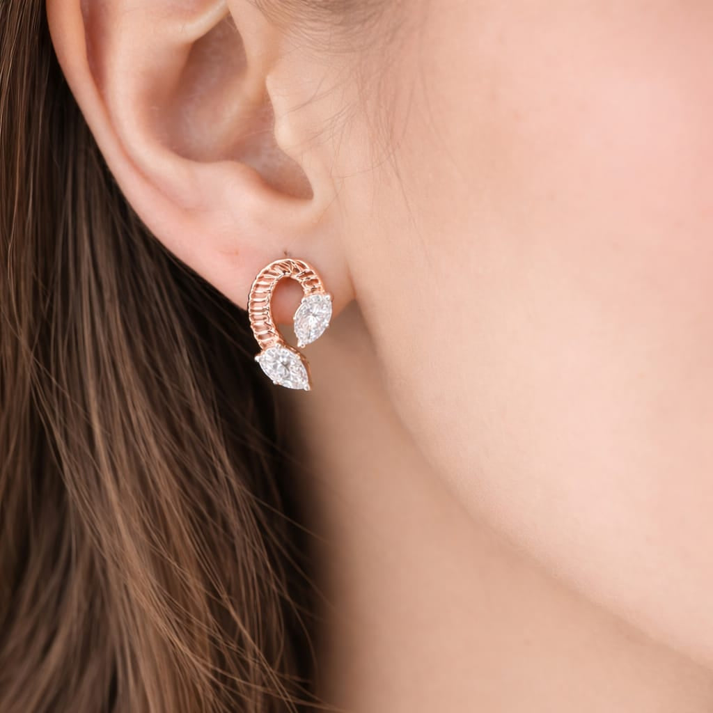 Rose gold earring with clear gemstones worn by a person with brown hair.
