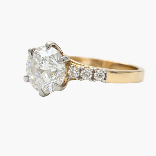 Gold ring with a large diamond and smaller diamonds on the band against a white background