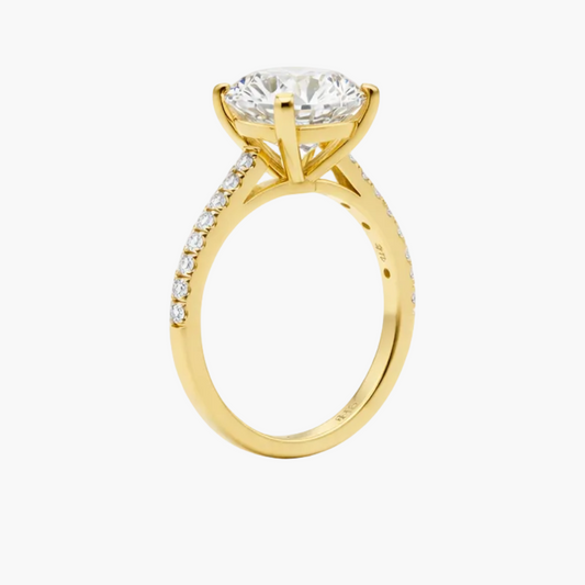 Gold ring with a large diamond and smaller diamonds on the band against a white background