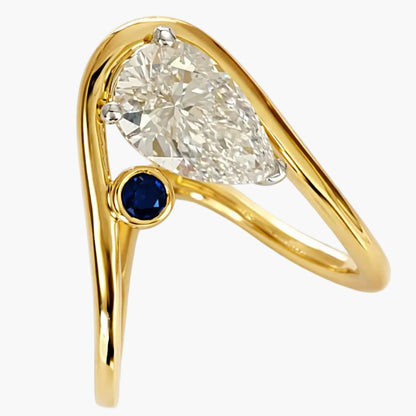 Gold ring with pear-shaped diamond and blue gemstone on a white background