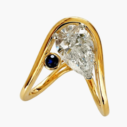 Gold ring with a diamond and blue gemstone on a white background