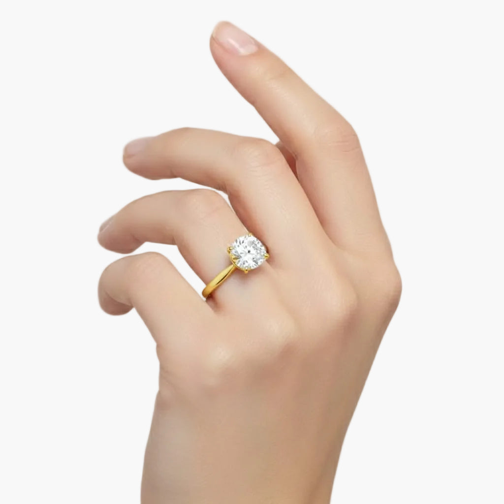 Gold ring with a diamond on a hand against a light gray background