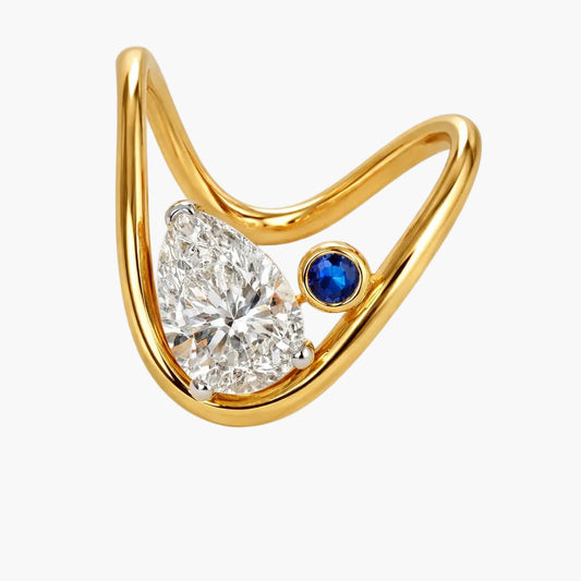 Gold ring with a pear-shaped diamond and a blue gemstone on a white background