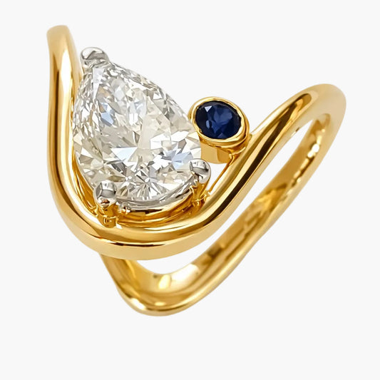 Gold ring with a pear-shaped diamond and a blue gemstone on a white background