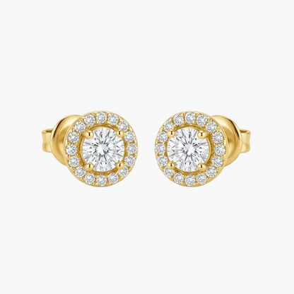 A pair of yellow gold stud earrings with a halo design, featuring a central round clear gemstone surrounded by a border of smaller clear stones, set against a plain light gray background.
