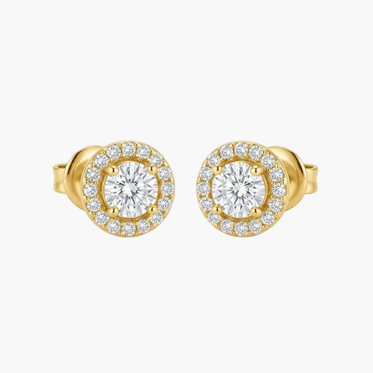 A pair of yellow gold stud earrings with a halo design, featuring a central round clear gemstone surrounded by a border of smaller clear stones, set against a plain light gray background.