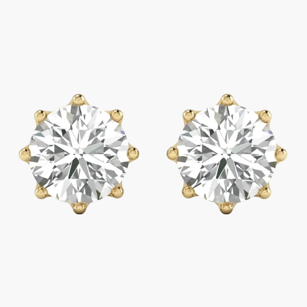 A pair of yellow gold stud earrings, each featuring a large round brilliant-cut diamond in a six-prong setting, shown against a plain white background.