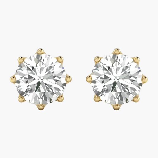 A pair of yellow gold stud earrings, each featuring a large round brilliant-cut diamond in a six-prong setting, shown against a plain white background.