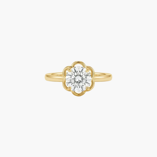 A yellow gold ring featuring a round-cut clear gemstone in a decorative floral or clover-like setting, centered on a plain light gray background.