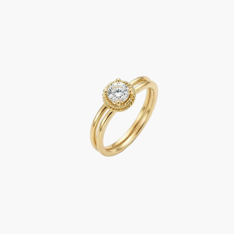 A gold ring with a round-cut clear gemstone in a bezel setting, accented by a halo of small diamonds and a textured outer border, shown on a plain white background.