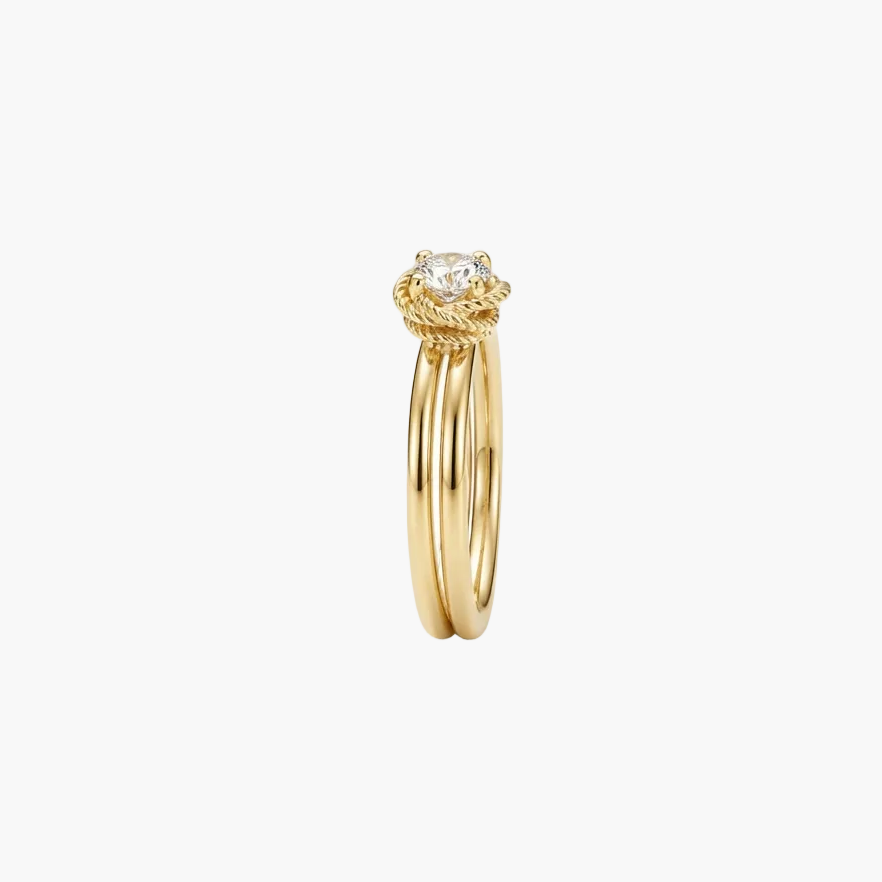 A gold ring with a twisted rope-style top and a single round clear gemstone, shown on a plain light gray background.