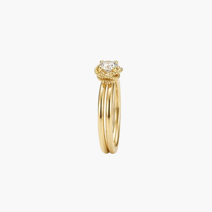 A gold ring with a twisted rope-style top and a single round clear gemstone, shown on a plain light gray background.