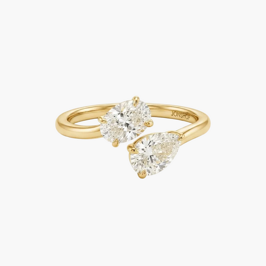 A gold ring with two pear-cut diamonds, one in a prong setting and the other in a bezel setting, on a clean white background. The brand name 'JONSPR' is engraved inside the band.