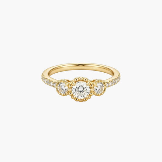 A yellow gold three-stone ring featuring a central round brilliant-cut diamond flanked by two smaller round diamonds, with small pavé diamonds along the shoulders, set against a clean white background.
