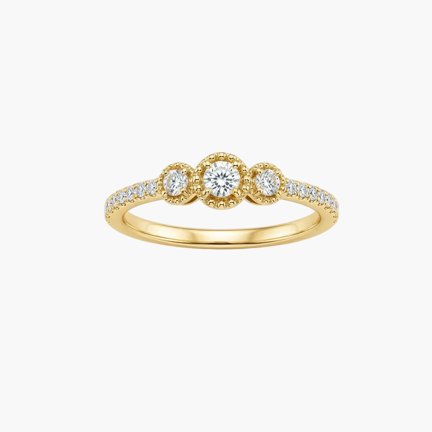 A yellow gold three-stone ring with a central round-cut diamond and two smaller oval-cut diamonds in halo settings, accented by pavé diamonds on the band, shown on a light gray background.