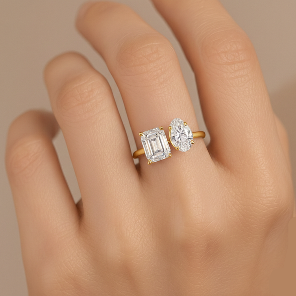 Gold ring with emerald-cut and round diamond on a hand against a neutral background