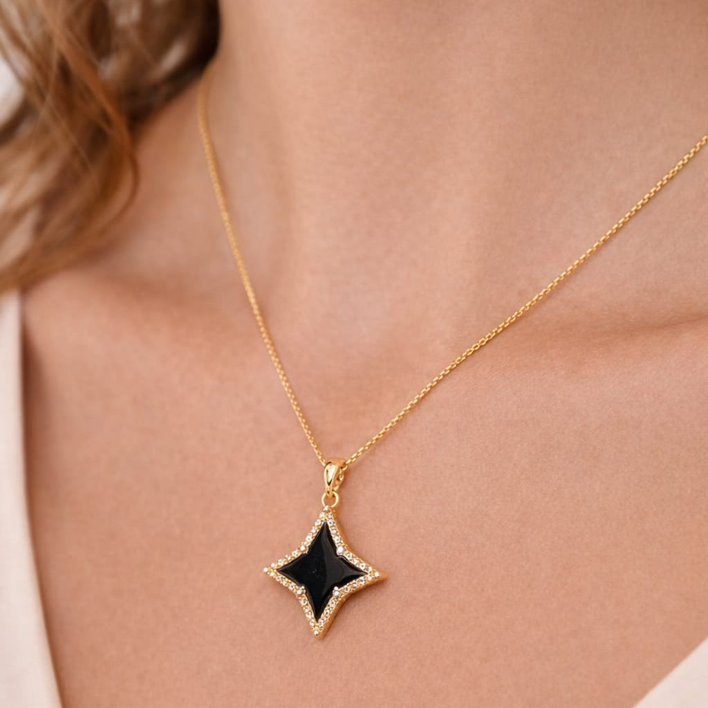 Gold necklace with a black star pendant on a person wearing a light-colored top.