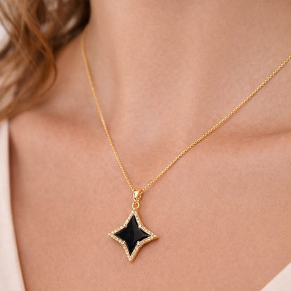 Gold necklace with a black star pendant on a person wearing a light-colored top.