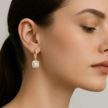 Close-up of a woman wearing gold earrings with a clear gemstone on a neutral background