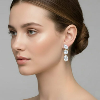 Close-up of a woman wearing a set of diamond earrings against a neutral background