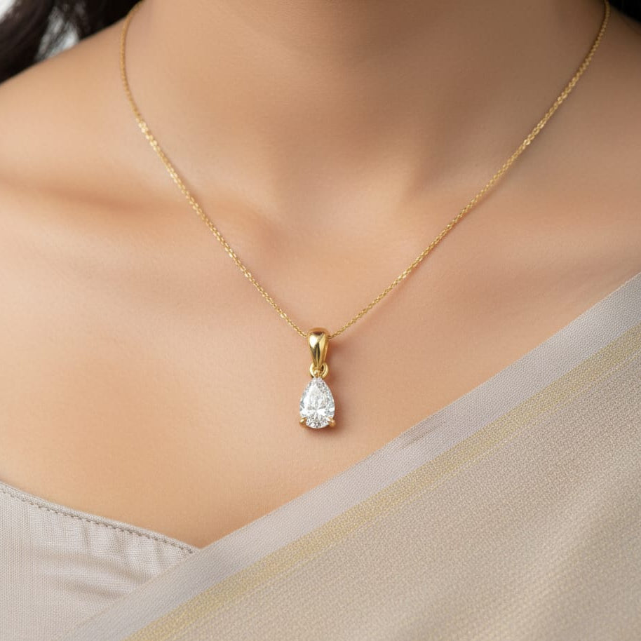 Gold necklace with a teardrop-shaped diamond pendant on a neutral background