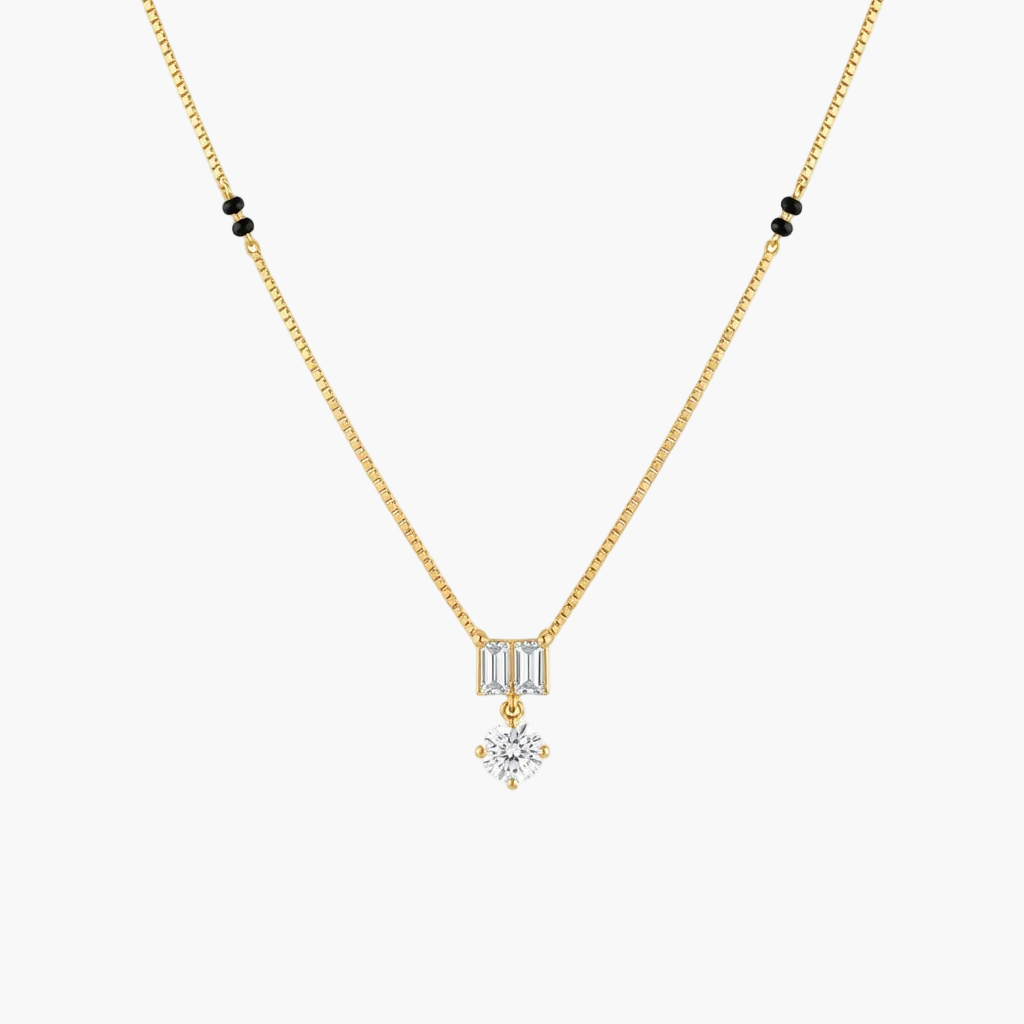 A delicate gold chain necklace featuring a small rectangular baguette-cut clear stone pendant, with a dangling round clear gemstone below, accented by small black beads on the chain against a white background.
