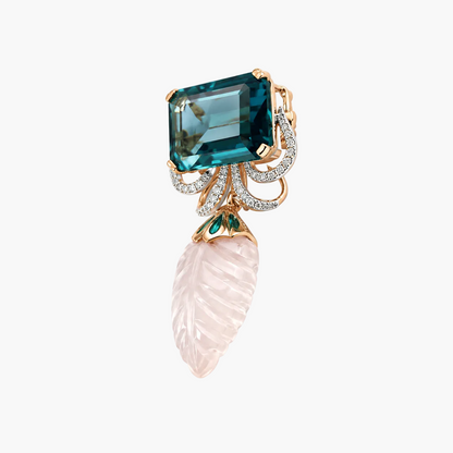 A luxury jewelry piece featuring a rectangular emerald-cut teal topaz, a carved pale pink rose quartz leaf dangle, and a rose gold setting accented with small white diamonds and a tiny green emerald.