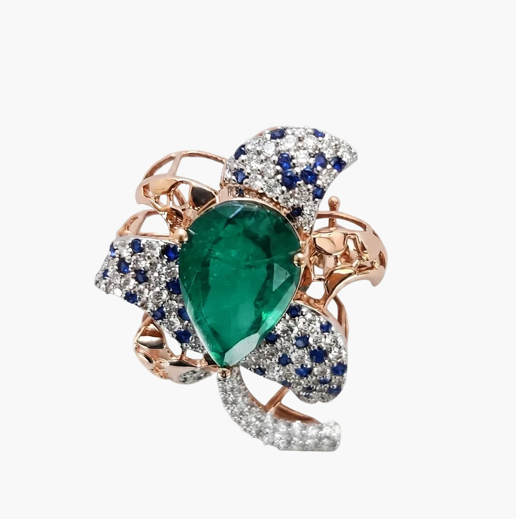 A rose gold ring featuring a large pear-cut green emerald center stone, surrounded by pavé-set blue sapphires and clear diamonds, on a clean white background.