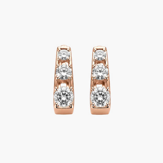 A pair of rose gold huggie hoop earrings with a channel setting of clear round-cut gemstones, shown against a plain white background.