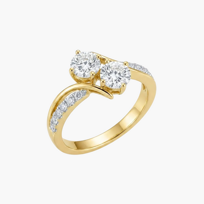 A yellow gold ring with two round-cut clear gemstones in a prong setting, accented by small pavé diamonds along a curved split shank, shown on a white background with a soft reflection.