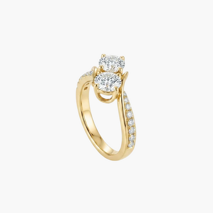 A yellow gold engagement ring featuring three round-cut diamonds, with a pavé-set diamond band, shown on a clean white background with a soft reflection.