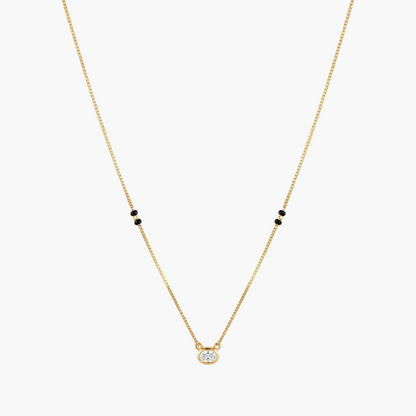 A delicate gold chain necklace featuring a small round clear gemstone pendant at the center and pairs of tiny black beads spaced along the chain, shown against a plain white background.