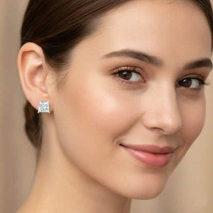 Close-up of a woman wearing diamond stud earrings with a neutral background