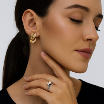 Women wearing gold earrings and a silver ring on a plain background