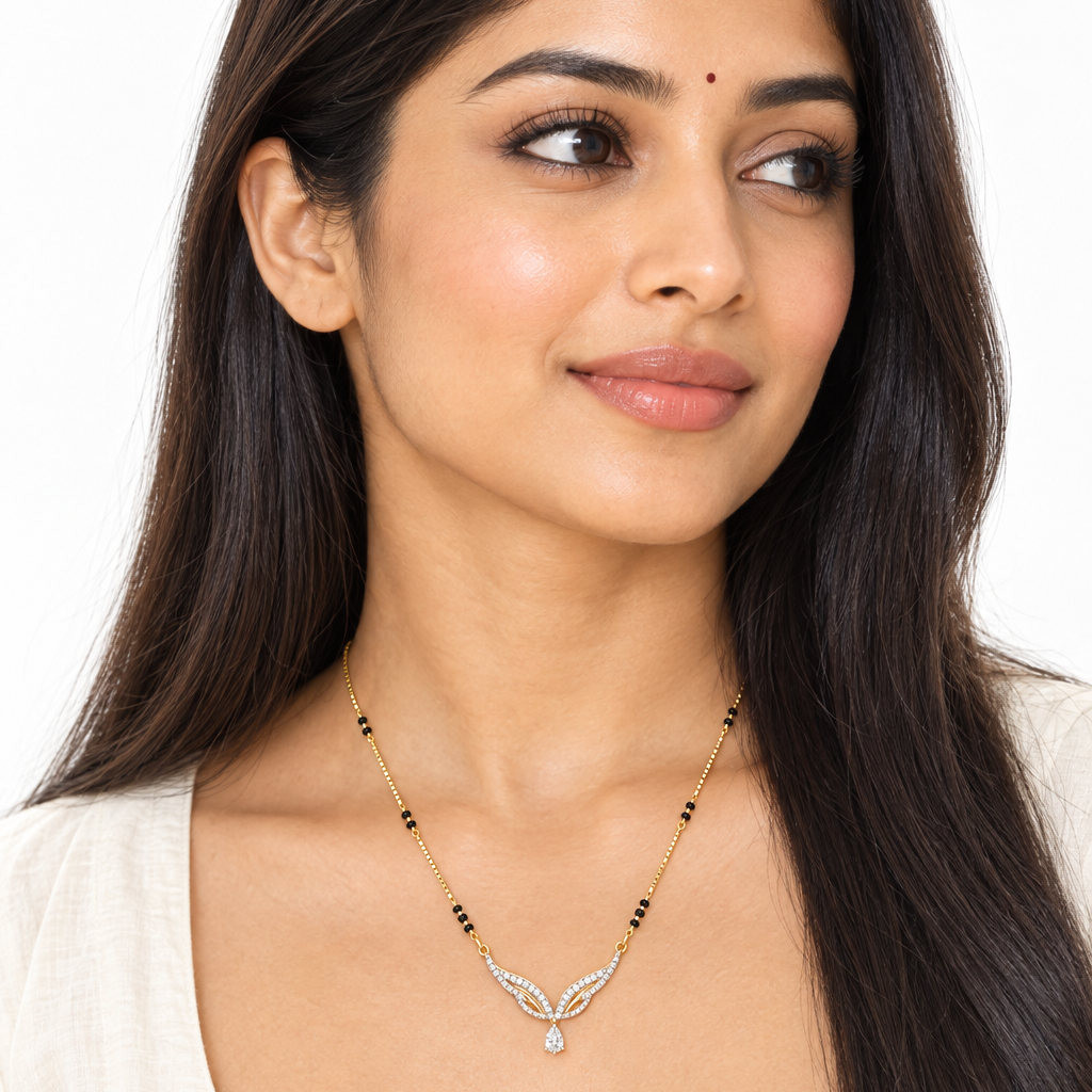 Beautiful elegant Indian female model with warm golden skin and long sleek straight hair worn loose over both shoulders wearing a very small delicate modern diamond mangalsutra featuring a fine yellow gold box chain with small traditional black beads meeting an elegant angel wing pendant — two symmetrical wings each composed of two layered open curved arcs both fully set with continuous rows of round brilliant diamonds in shared pavé prong settings with a thin open yellow gold channel between the arcs creat