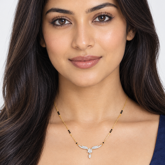 Beautiful elegant Indian female model with warm light golden skin and sleek straight hair falling over both shoulders wearing a very small delicate modern diamond mangalsutra featuring a fine yellow gold box chain with small traditional black beads scattered at intervals meeting a breathtaking butterfly bird wing pendant — two gracefully curved wing-shaped arms fully set with continuous rows of round brilliant diamonds in shared pavé prong settings sweeping outward and upward from a central diamond floral r