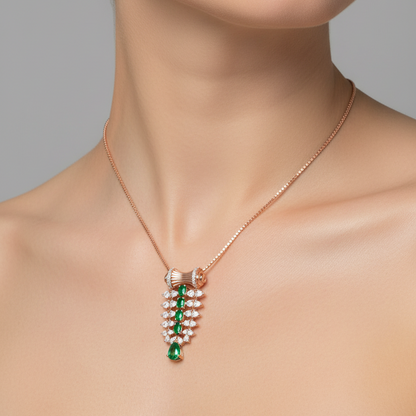 A close-up of a model wearing a delicate rose gold necklace with a pendant featuring green emerald-cut stones and white pearl-like accents, set against a solid gray background.