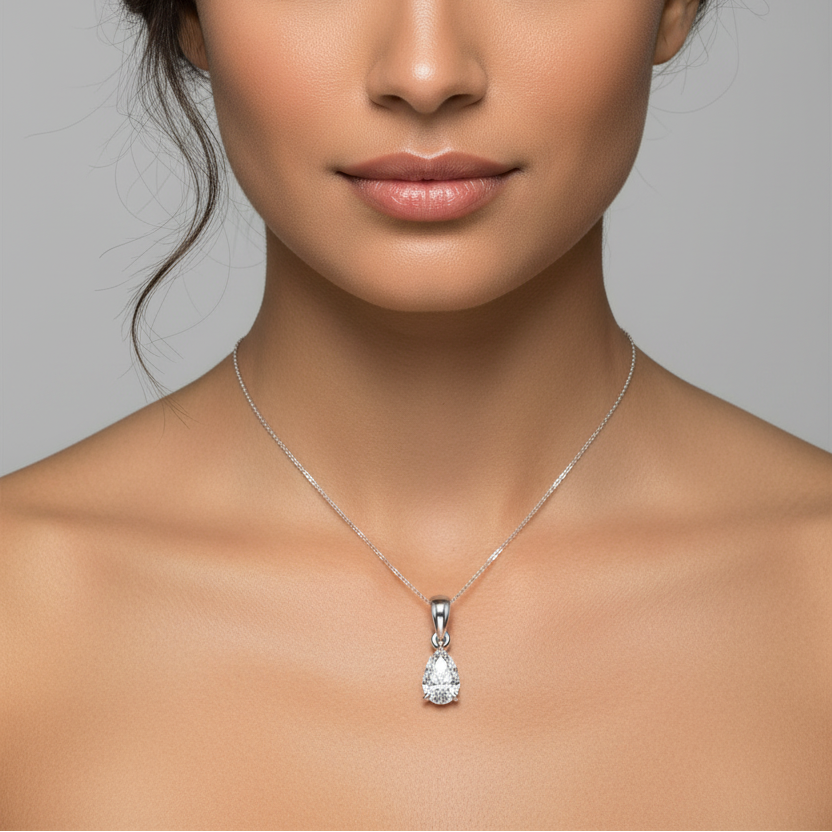 Female model wearing small white gold pear-cut diamond solitaire pendant with three-prong setting, rounded arch bail and jump ring connector on fine white gold chain