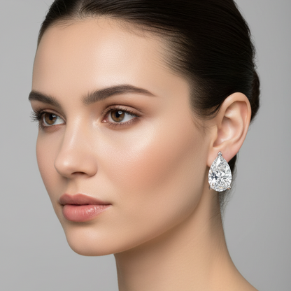 Female model wearing small white gold pear-cut diamond solitaire stud earrings with distinctive five-prong setting — one angular triangular arrowhead prong at the top pointed tip and four double ball-tipped claw prongs at the rounded bottom