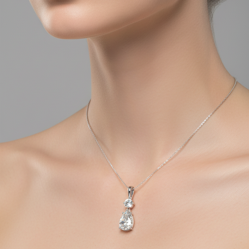 Female model wearing small white gold two-stone drop pendant with round brilliant and pear-cut diamonds