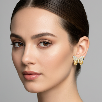 Female model wearing small yellow gold butterfly stud earrings with round brilliant micro-pavé diamond upper wings sparkling brilliantly and smooth plain yellow gold lower wings with deeply engraved radiating fan sunburst line texture sitting flush against the earlobe