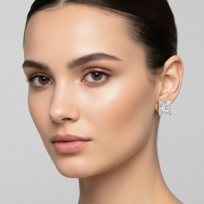 Female model wearing small yellow gold princess-cut diamond solitaire stud earrings with square corner prongs