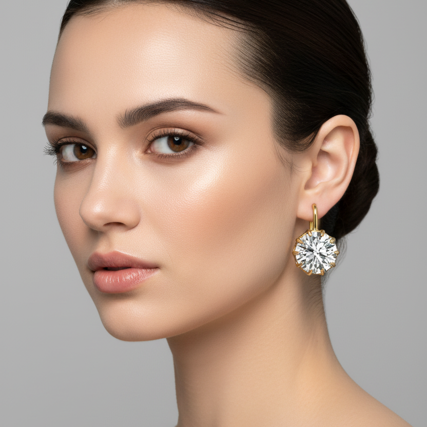 Female model wearing small yellow gold round brilliant diamond drop earrings with dramatic eight-prong double ball-tipped crown setting fanning outward like a starburst and slim polished yellow gold lever-back hook, the diamond hanging just below the earlobe