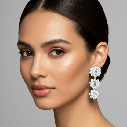 Female model wearing very small white gold three-tier graduating diamond flower cluster drop earrings with three circular snowflake flower clusters of round brilliant diamonds cascading from largest at top to smallest at bottom connected by tiny white gold links
