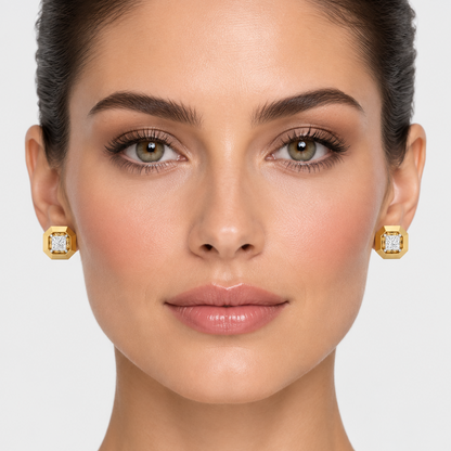 Female model wearing very small yellow gold architectural octagonal princess-cut diamond stud earrings with a wide thick high-mirror polished regular octagon outer frame featuring chamfered angled edges between each flat polished face with a deep square recessed channel cavity cut into the center interior walls angled and faceted creating a brilliant reflective inner surround around a large princess-cut diamond in four white gold ball-tipped corner prong settings sitting flat and compact against the earlobe