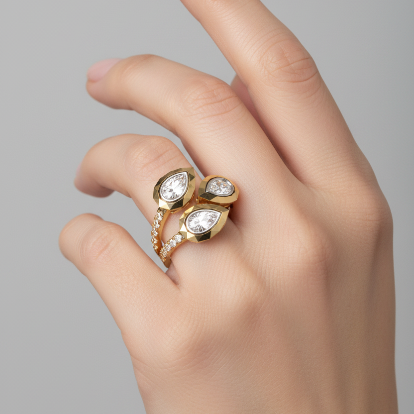 Female model wearing very small yellow gold three-stone geometric faceted bezel cluster ring with pear-cut diamonds and double pavé split band