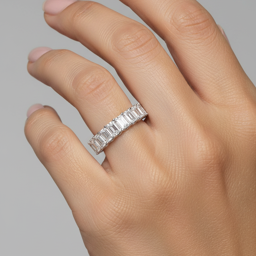 Female model wearing white gold emerald-cut diamond half-eternity wedding band with east-west set rectangular step-cut diamonds in scalloped shared claw prong settings across the top of the finger on a smooth plain white gold band