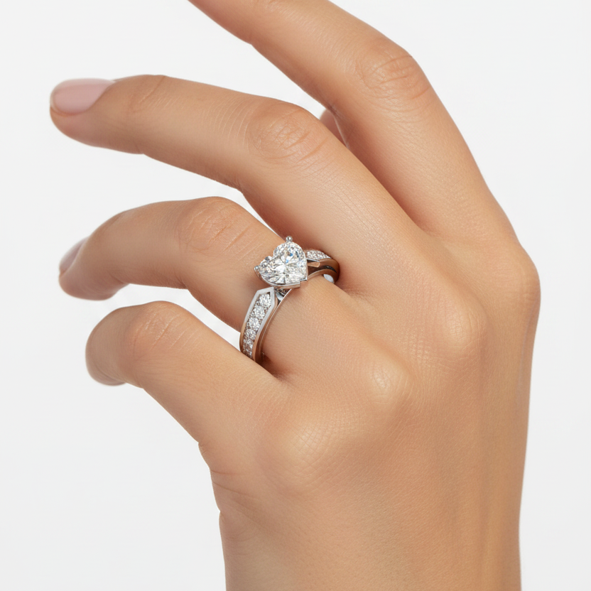 Female model wearing white gold heart-cut diamond solitaire engagement ring with three-prong setting, geometric chevron shoulder brackets and wide channel-set round brilliant diamond band on both shoulders